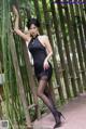 A woman in a black dress posing in front of a bamboo fence.